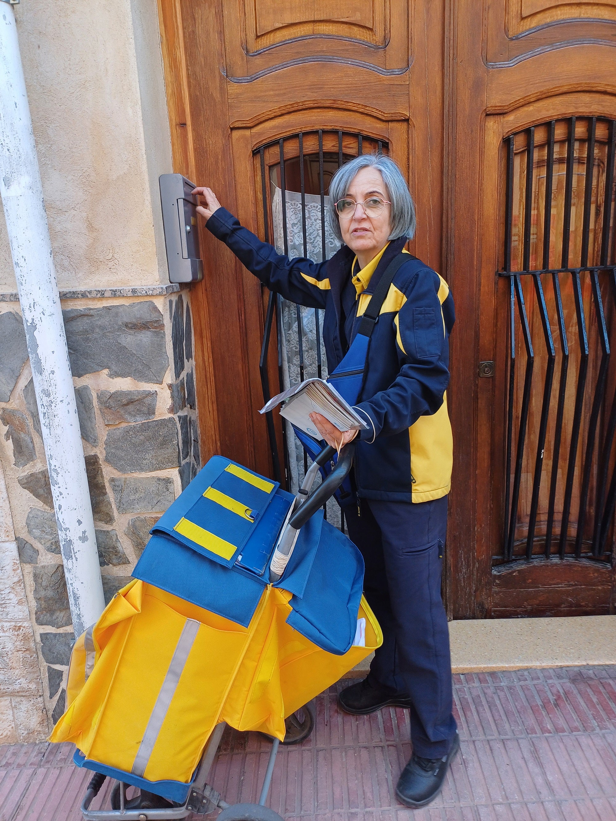 Imagen secundaria 2 - Arriba, Mª Carmen atiende a una cliente en la oficina. Sobre estas líneas, en su recorrido por el mucipio entregando paquetes, notificaciones y alguna que otra carta.