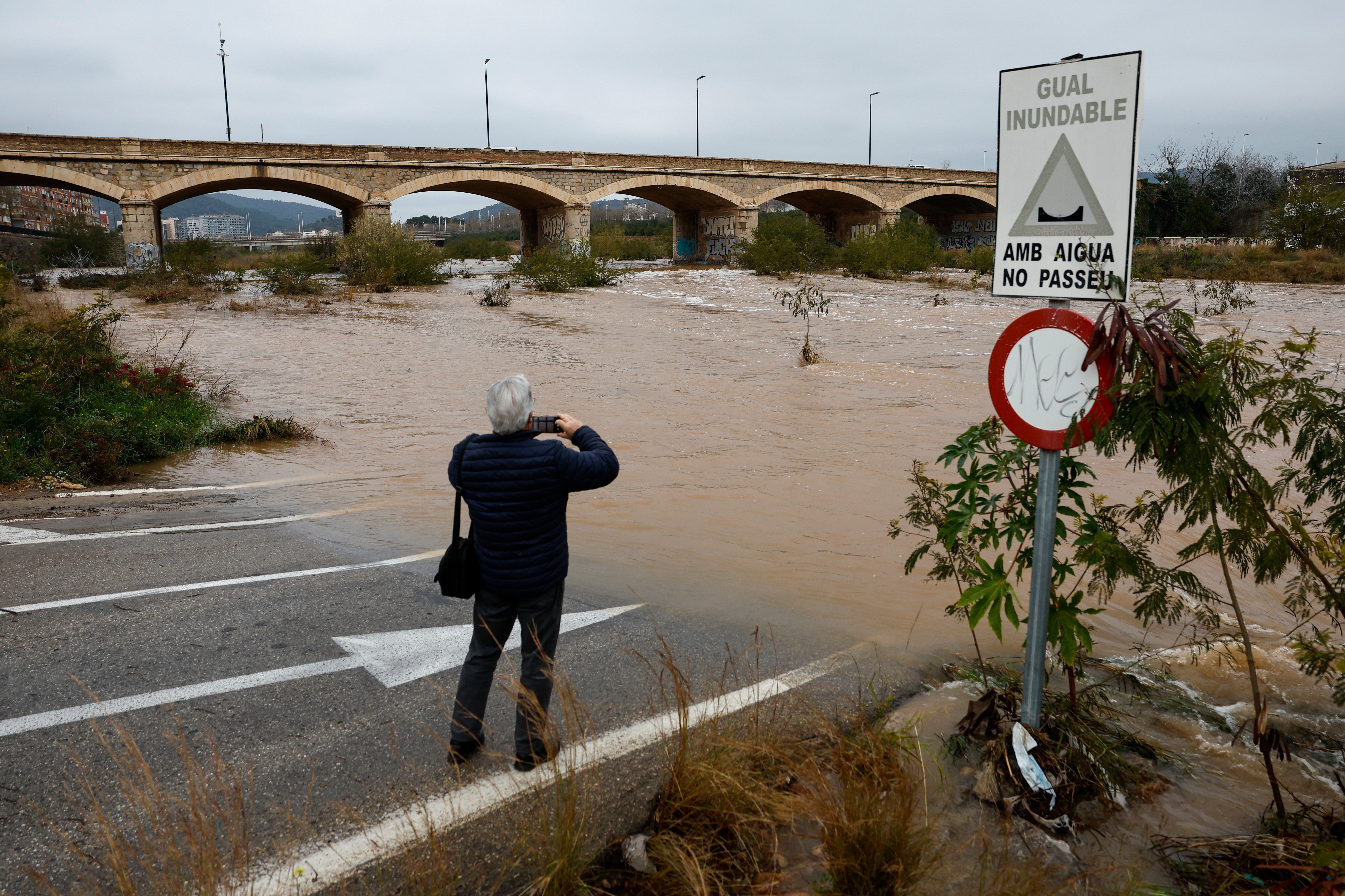 Un hombre fotografía la crecida del río Palancia y una carretera anegada a su paso por Sagunto