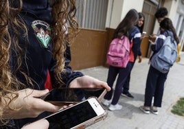 Unos jóvenes miran el móvil en el entorno de un centro educativo.