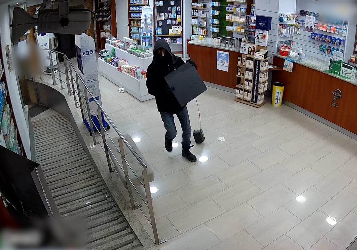 Uno de los delincuentes carga con la caja de una farmacia de Ribarroja, en un asalto captado por la cámara de seguridad.