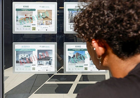 Un joven observa los pisos en alquiler en el escaparate de una inmobiliaria.