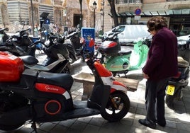 Una mujer rodeada de motos situadas en la acera de la calle Poeta Querol, frente al Palacio del Marqués de Dos Aguas.