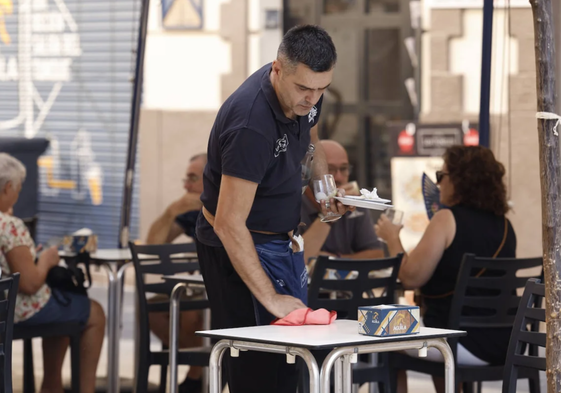 Un camarero limpia la mesa de una terraza.