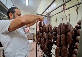 Un carnicero maneja unas ristras de embutido de apetitoso aspecto.