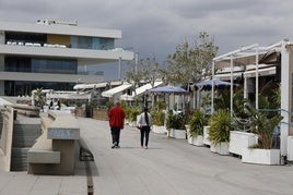 Dos personas pasean por el paseo frente a los restaurantes.