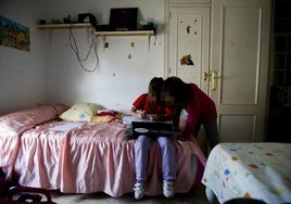 Dos niñas realizan los deberes sentadas sobre la cama de su habitación.