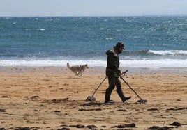 Un hombre busca objetos en una playa con un detector de metales.