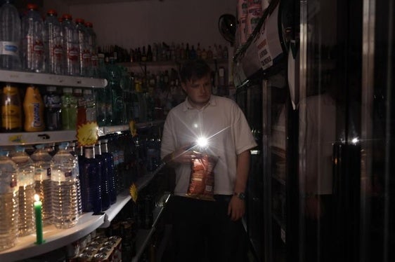 Un hombre se alumbra con la linterna del móvil en un supermercado, el día del apagón.