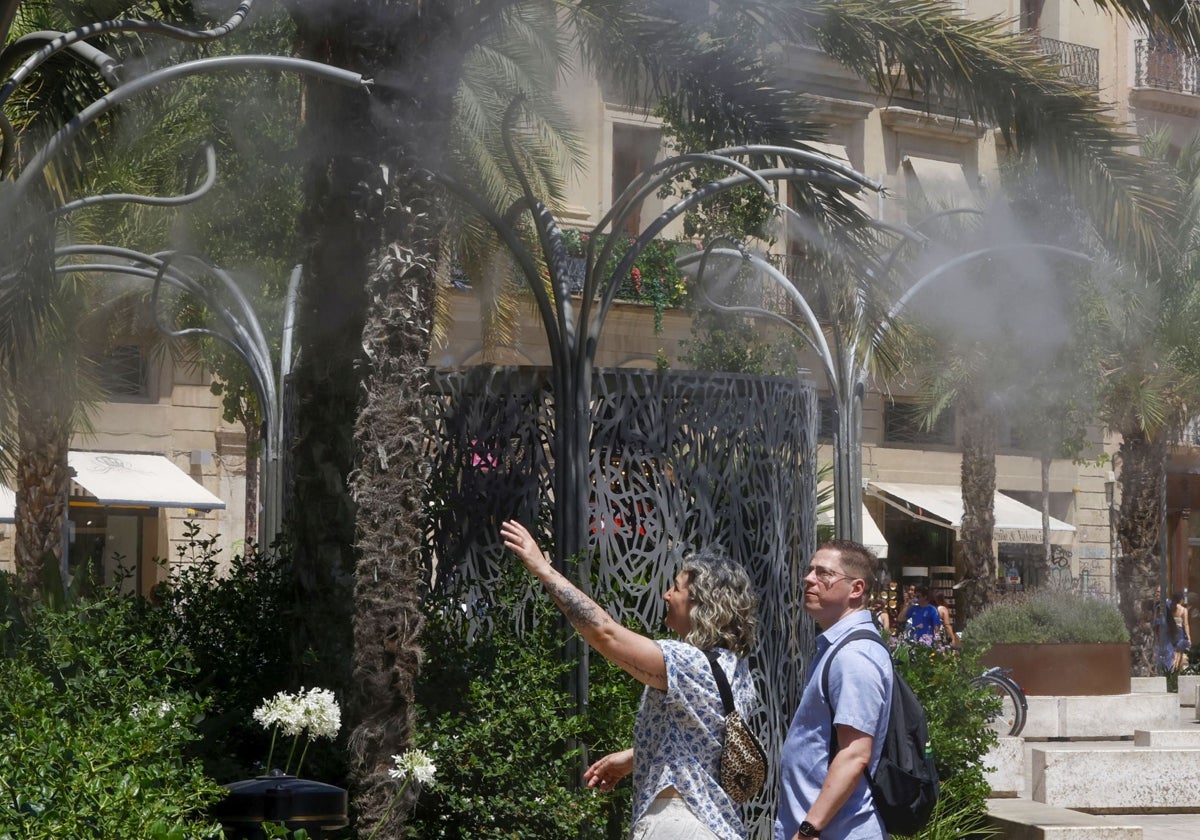 Un hombre y una mujer se refrescan en los aspersores de la plza de la Reina.