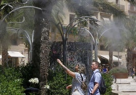 Un hombre y una mujer se refrescan en los aspersores de la plza de la Reina.
