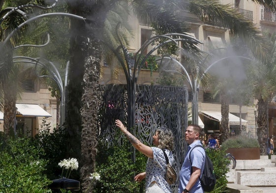 Un hombre y una mujer se refrescan en los aspersores de la plza de la Reina.