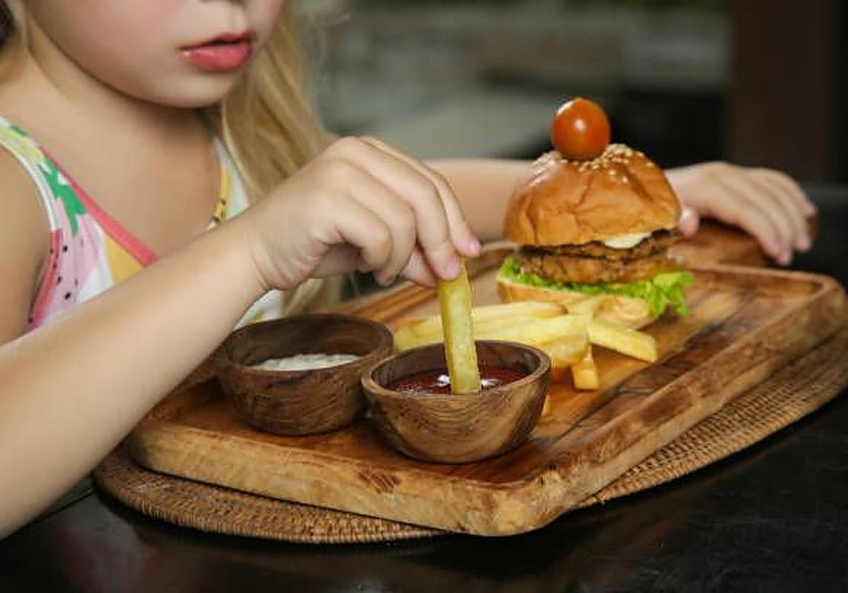 Una niña come una hamburguesa en un restaurante.