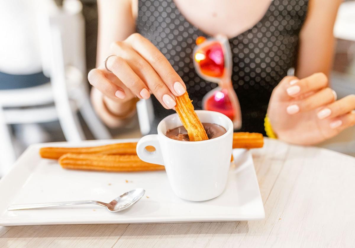 Una mujer moja churros en el chocolate