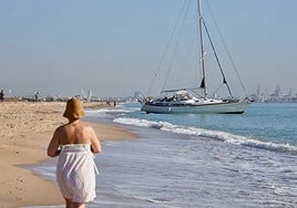 Una bañista pasea junto al velero varado en El Saler.