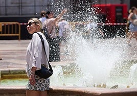 Una mujer trata de mitigar el calor junto a un chorro de agua.