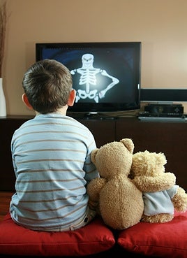Niño ve la televisión junto a dos muñecos de peluche