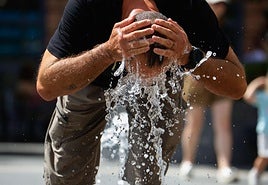 Un hombre refrescándose en una fuente durante una ola de calor.