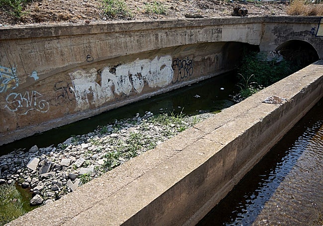 La acequia paralela a la V-30, aún con maleza y escombros de la dana.