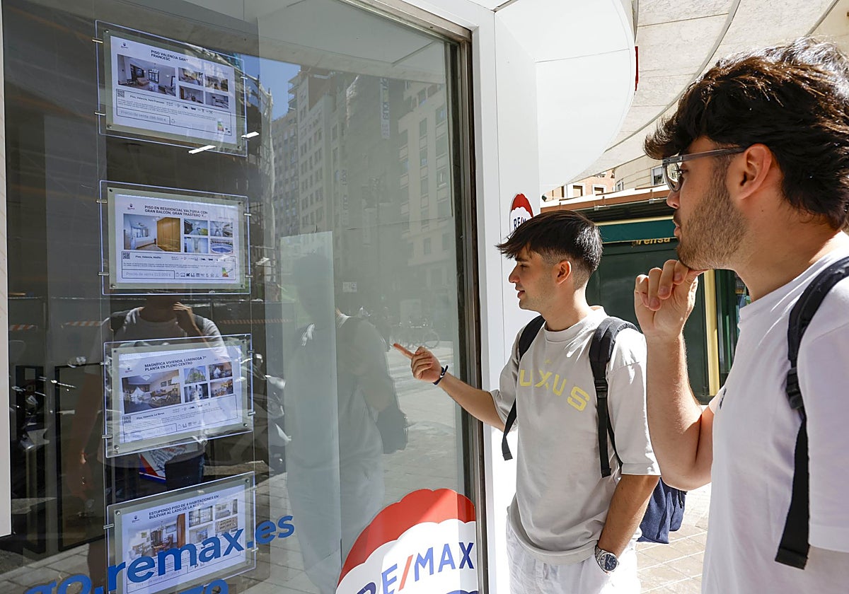 Dos jóvenes observan la oferta de pisos en una inmobiliaria.