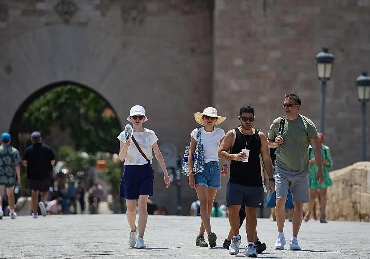 Turistas pasean por Valencia equipados con sombreros y abanicos para combatir el calor.