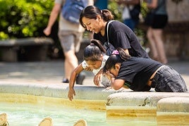 Varias personas se refrescan en una fuente.