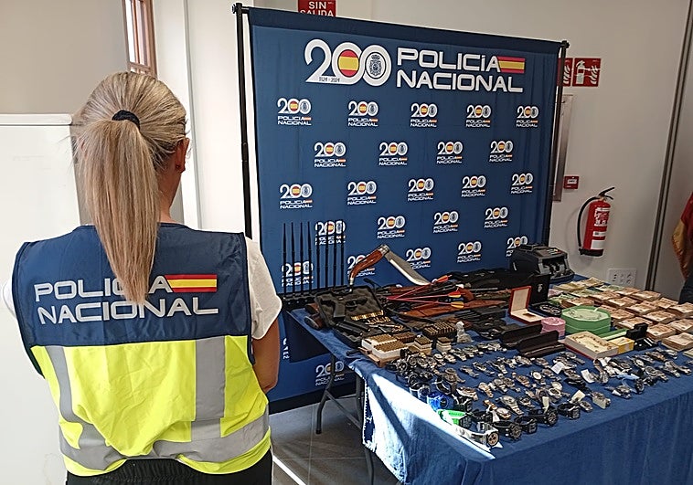 Una policía junto a las armas, dinero, munición y relojes intervenidos a los detenidos.