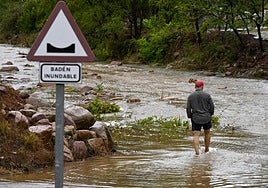 Un hombre trata de cruzar el cauce de una rambla esta mañana.