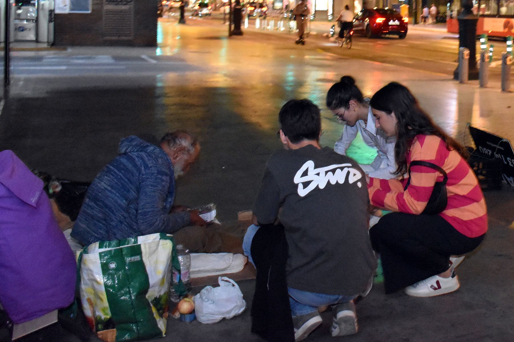Un grupo de universitarios entregan una cena y hablan con una persona sin techo.