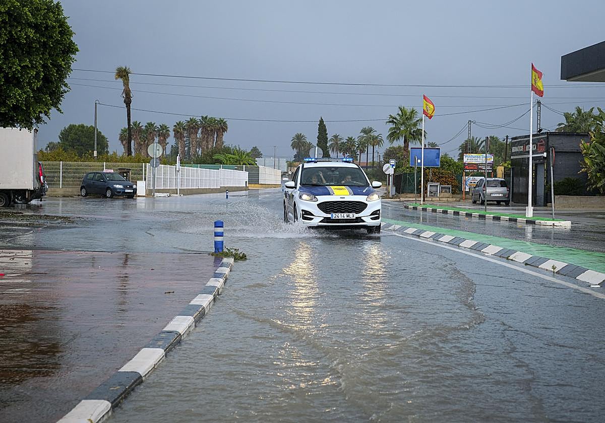 Un coche de policía circula por una calle anegada por la lluvia en Foia, en Elx.