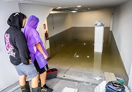 Dos vecinos de los adosados inundados en Alcàsser observan como después de vaciar el garaje se les ha vuelto a llenar de agua.