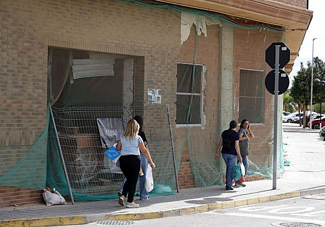 Un grupo de viandantes pasan junto a una finca con la huella de la dana.