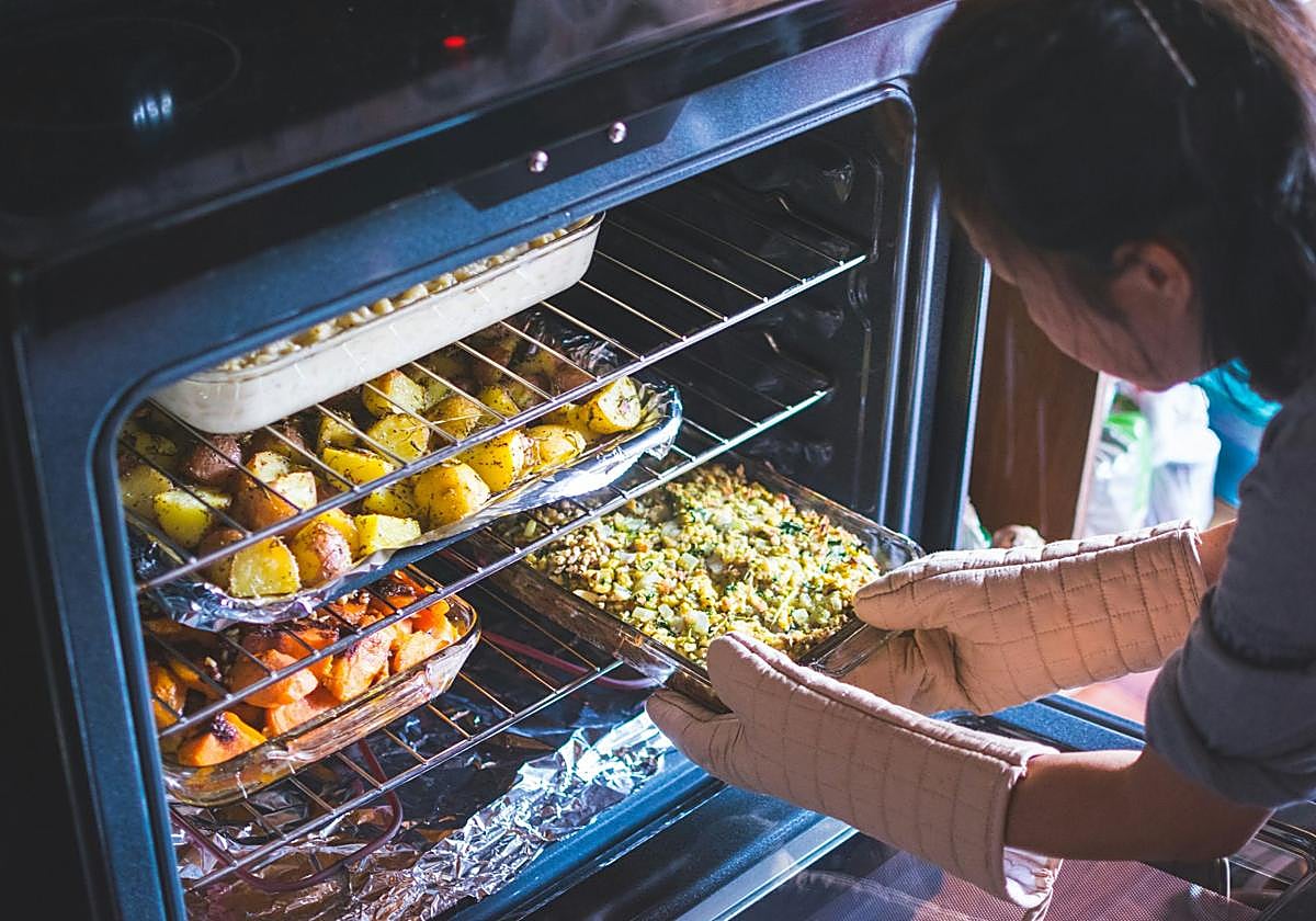 Una mujer coloca diferentes bandejas en un horno.