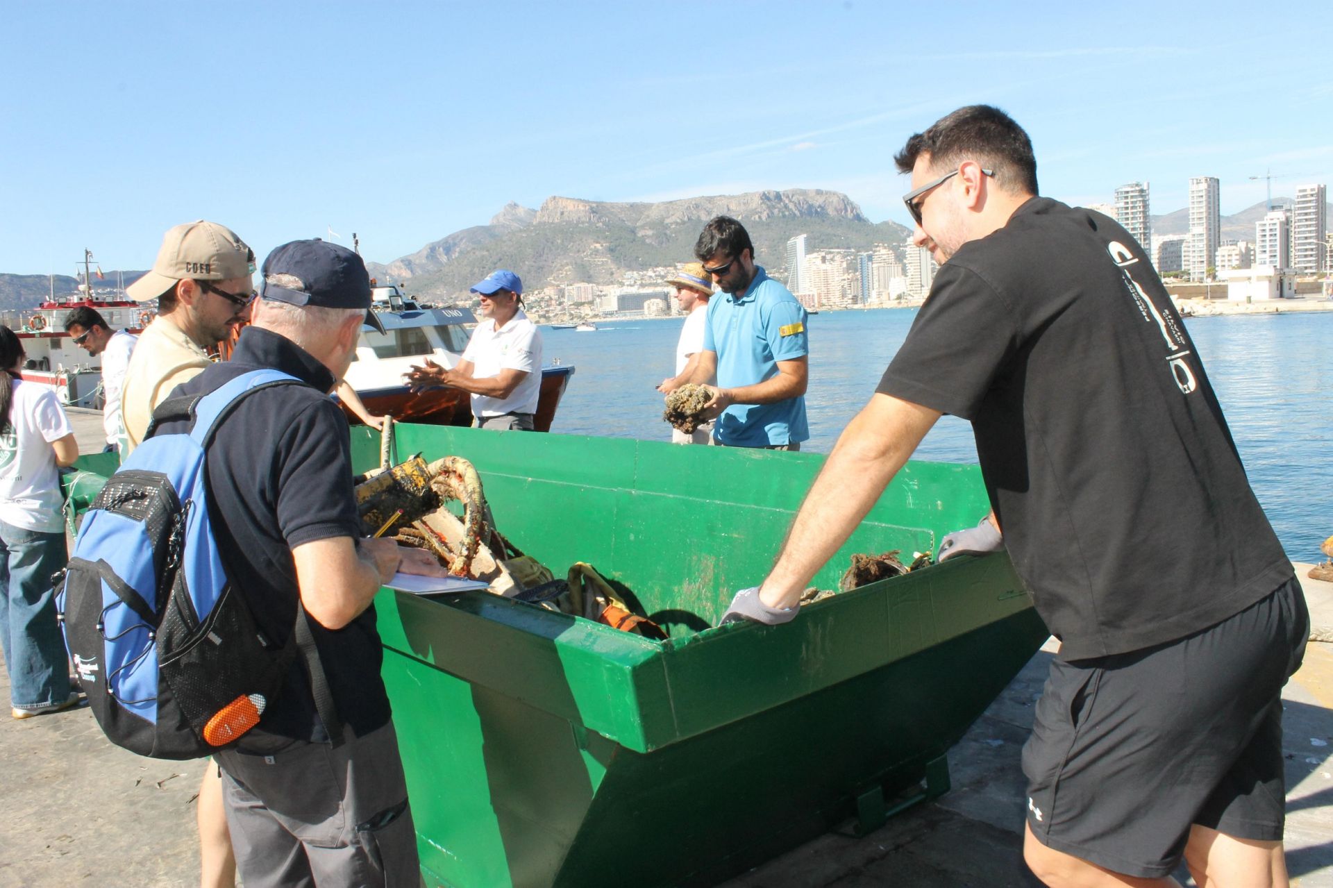 Vluntariado junto a un contenedor con residuos.