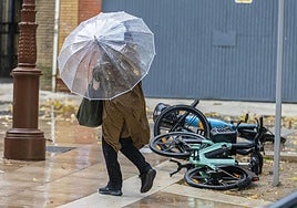 Una mujer con paraguas pasa ante unas bicicletas caídas.