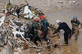 Varios agentes del GEA de la Guardia Civil inspeccionan un vehículo arrastrado por la riada.