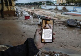 Un hombre sostiene un móvil en medio de una Catarroja embarrada con el Es-Alert que mandó Emergencias a las 20.11 horas del 29 de octubre de 2024.