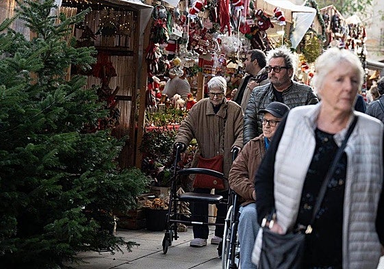 Varias personas pasean por un mercadillo navideño.