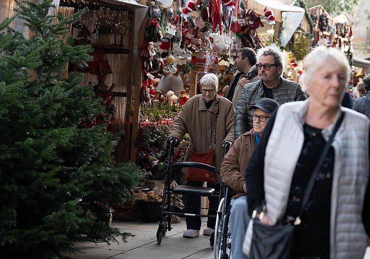 Varias personas pasean por un mercadillo navideño.