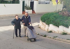 Vicenta se coge al brazo de Antonio, que le ayuda a subir la rampa con el carro de la compra.
