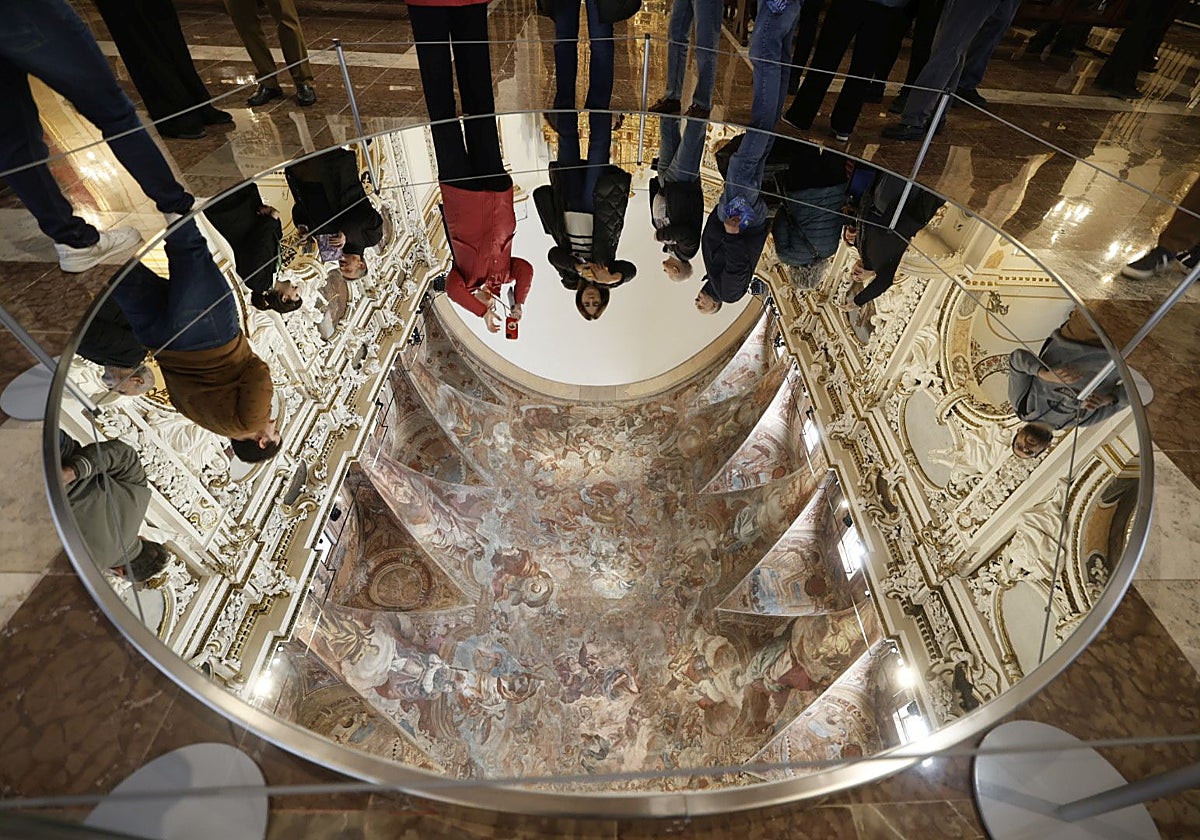 Visitantes observan los frescos de Palomino a través del espejo que se ha instalado en el piso.