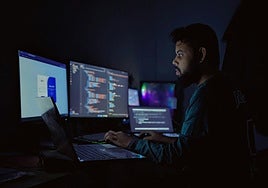 Un hombre trabaja frente a varios ordenadores durante la noche.