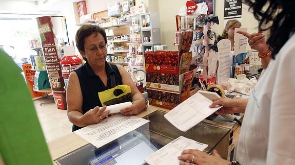 La clienta de una farmacia es atendida por una trabajadora que observa sus recetas. 