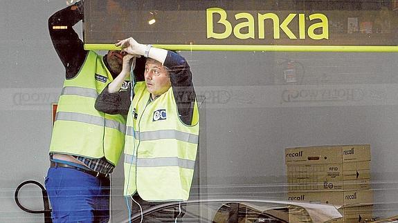 Dos trabajadores colocan un cartel de Bankia en una de sus oficinas.