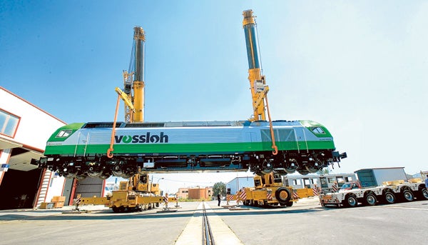 Dos grúas cargan una locomotora de Vossloh España para su transporte por carretera.