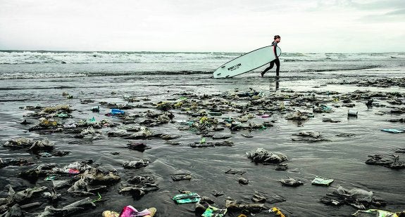 Una surfista camina por una playa repleta de desechos.