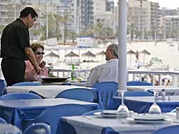 Un camarero atiende a una pareja en un restaurante de la playa de Gandia.