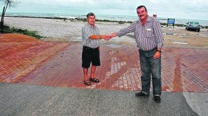 VECINOS. Dos residentes en la playa de l'Almadrava se estrechan la mano en la calle que divide los términos de Dénia (izquierda) y Els Poblets (derecha). /JOSÉ IGLESIAS