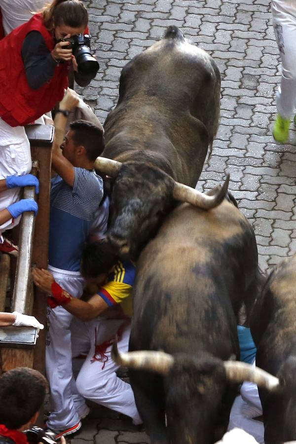 Un toro alcanza a dos mozos que intentan protegerse contra la pared.