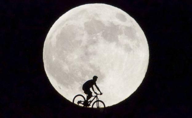 Un ciclista pasa delante de la Luna llena.