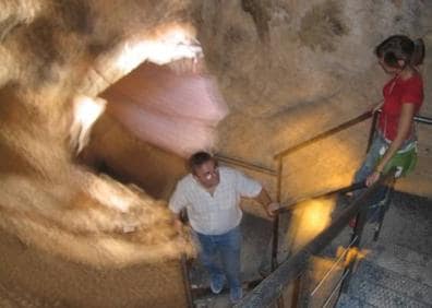 Imagen secundaria 1 - Un hombre abriendo la entrada a la Cueva de la Serreta, las escaleras de bajada a la misma, y tres visitantes en la terraza volada sobre el cañón.